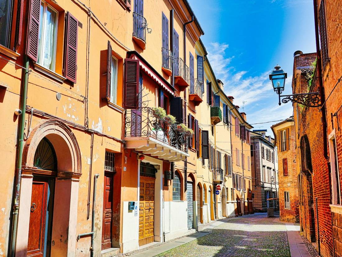 Ferrara attractions – colorful medieval street with cobblestones, orange houses and wooden shutters in Italy