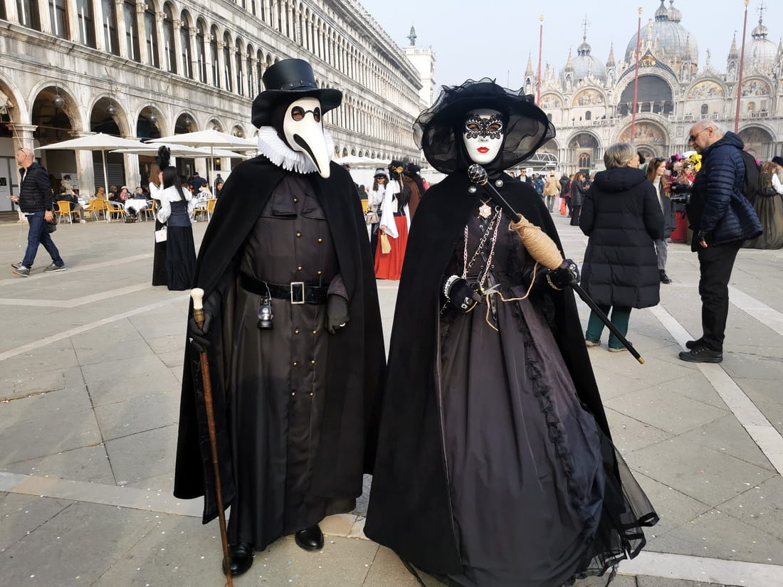 Venice Carnival participants dressed as a Plague Doctor and a dark noble lady in Piazza San Marco