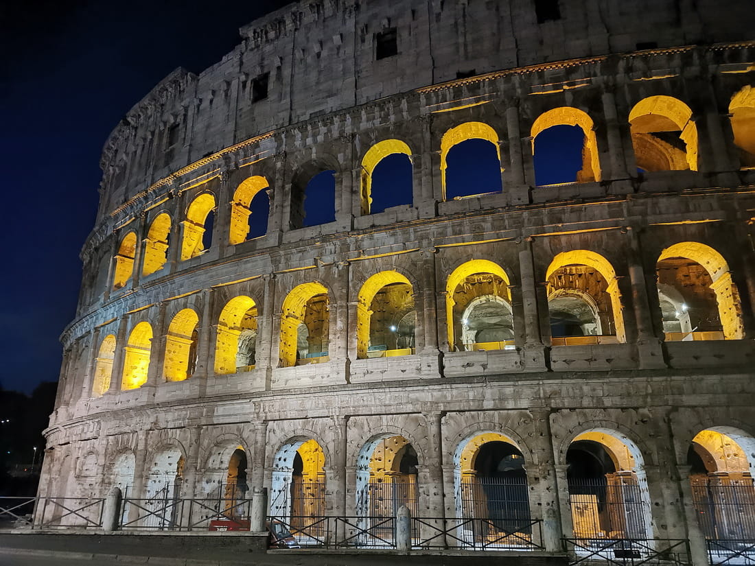 The Colosseum in Rome illuminated at night against a dark blue sky
