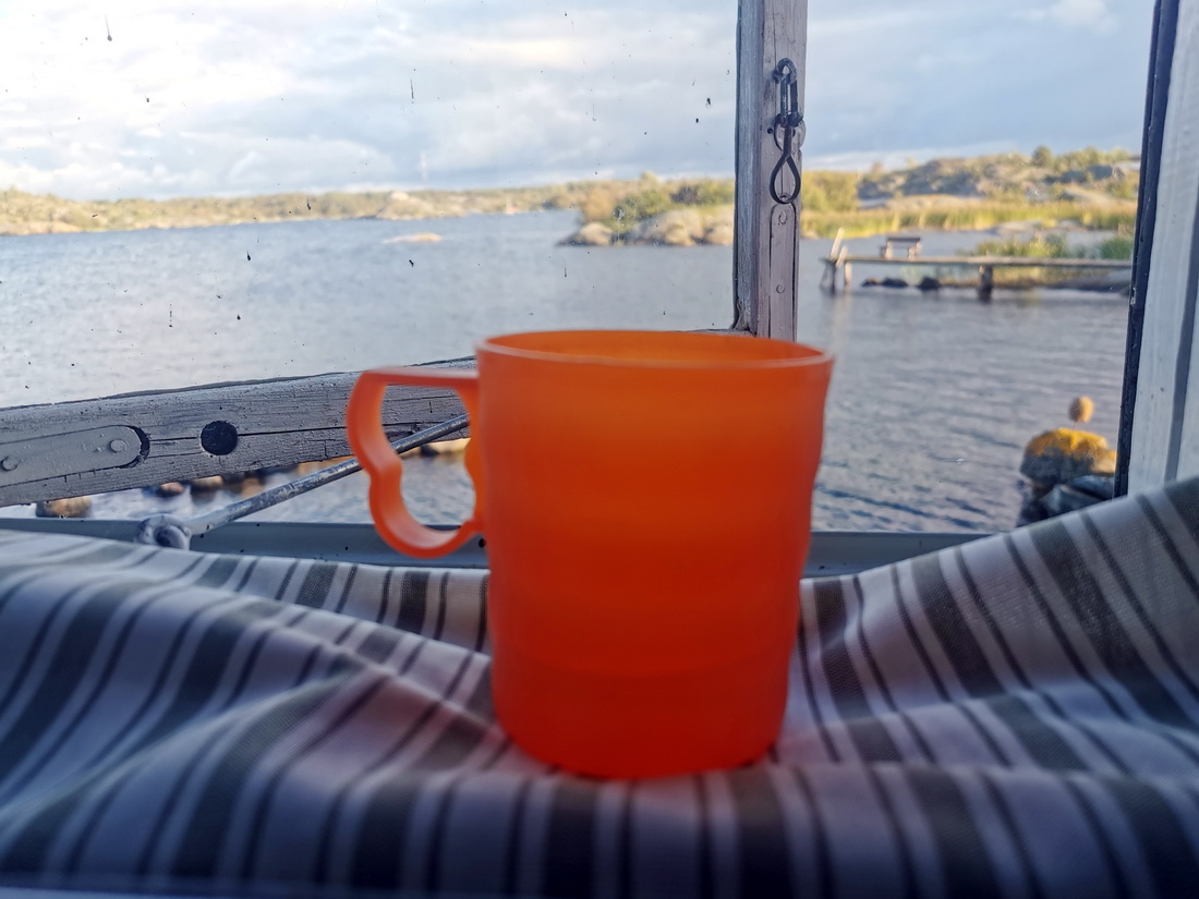 Orange coffee mug on a window sill overlooking the Baltic sea in Åland