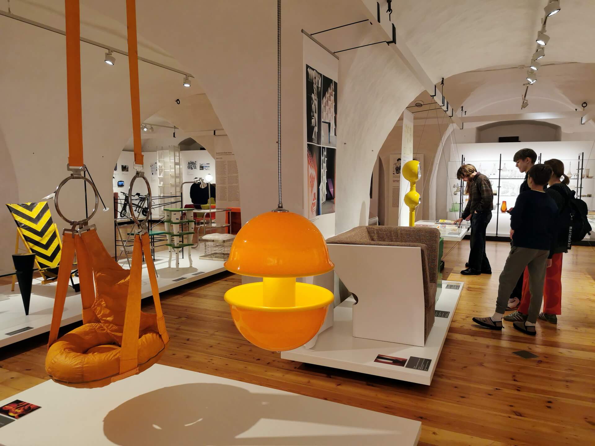 Interior of the Estonian Museum of Applied Art and Design in Tallinn, featuring a bright orange retro-futuristic hanging chair beneath 17th-century vaulted ceilings