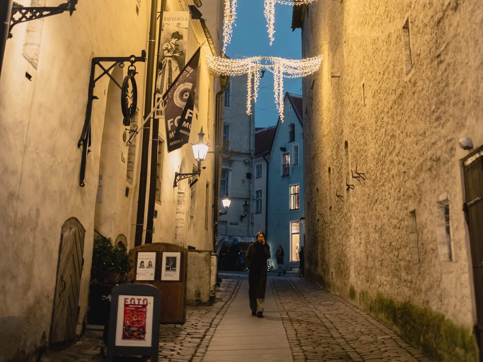 Exterior of the Museum of Photography in a narrow cobblestone alleyway in Tallinn Old Town at dusk, with banners reading Fotomuuseum and Raevangla