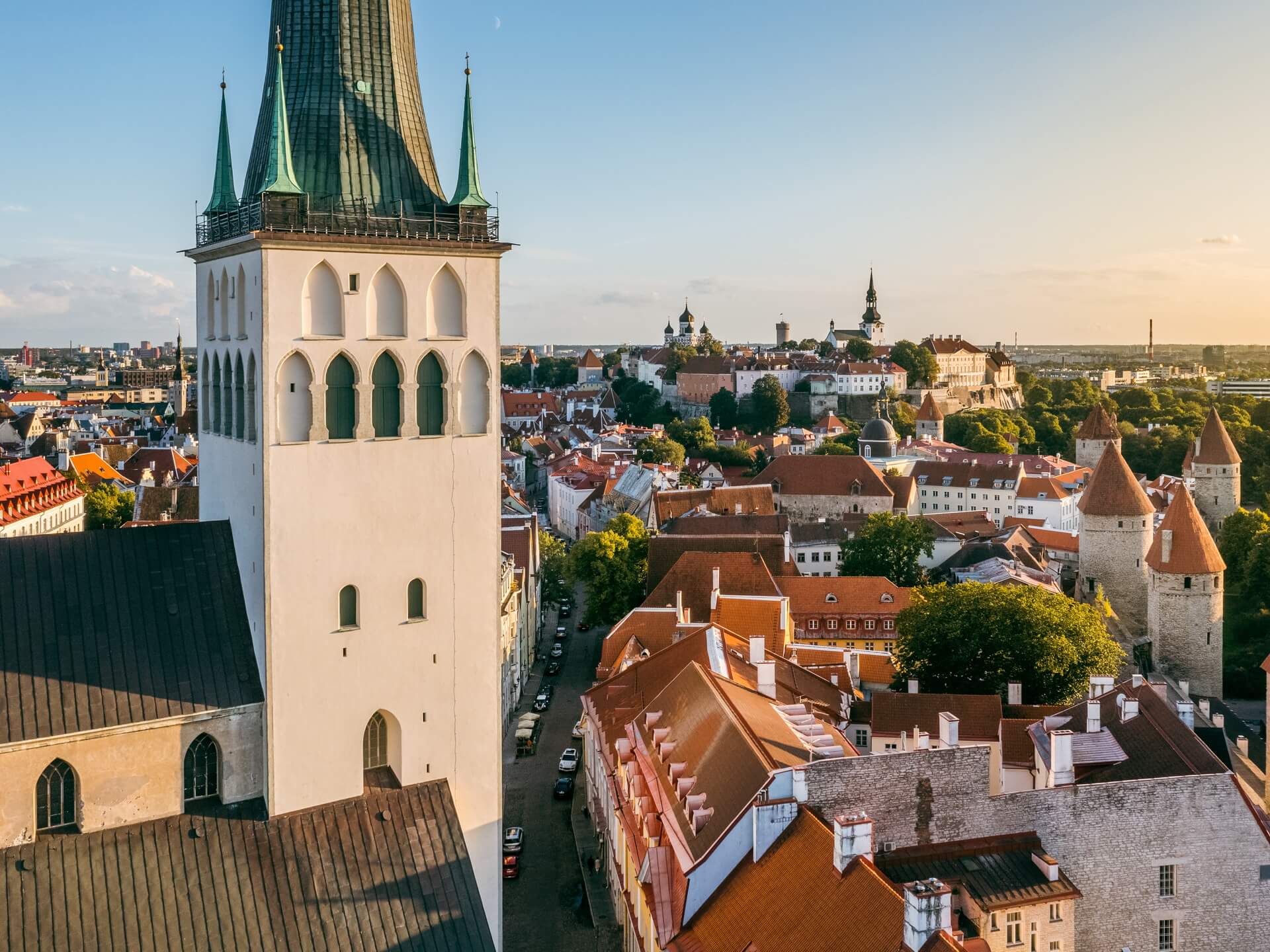Aerial view of St. Olaf's Church tower anchoring the Tallinn Old Town skyline with red roofs and Toompea hill in the background