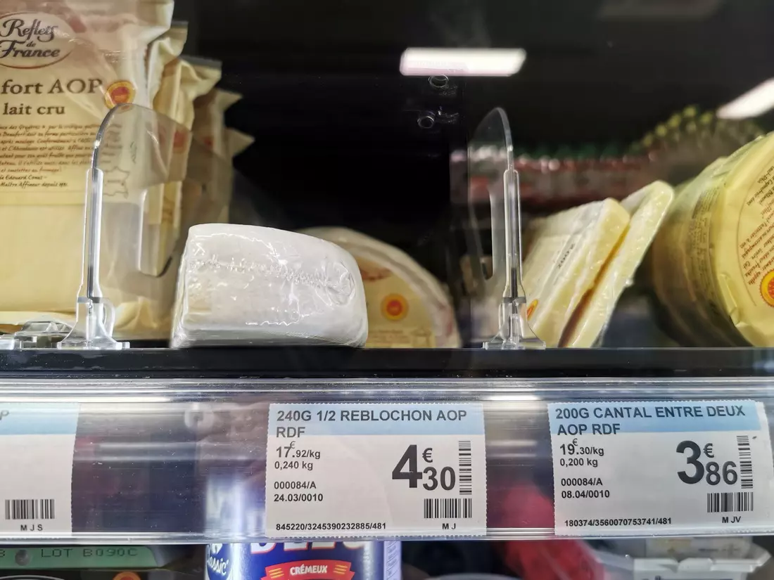 A display of French cheeses at a supermarket, featuring Reblochon AOP and Cantal entre deux AOP.