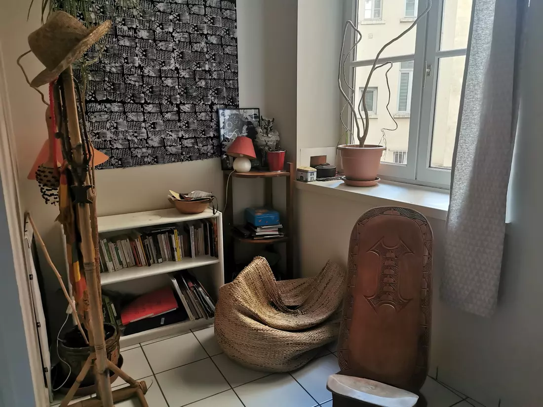 Cozy corner in a Lyon apartment with bookshelves, a beanbag chair, and African-inspired decor by a bright window.