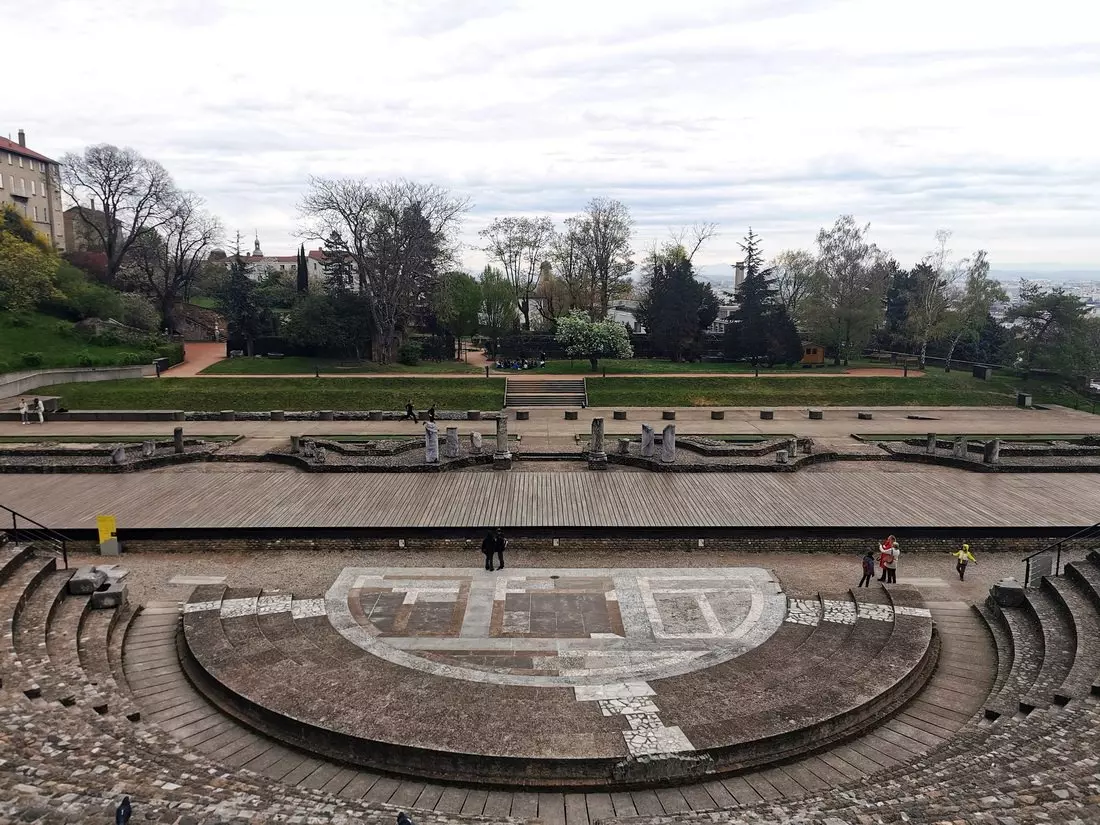 View of the Roman Theatre in Lyon on a cloudy day, showing tiered stone seating that gets very hot in summer sun.