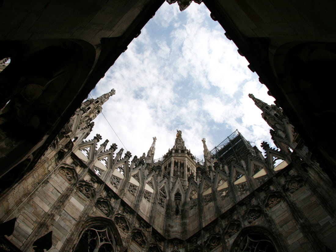 Low angle abstract view looking up at the sky framed by the dark gothic arches of Milan Cathedral rooftop