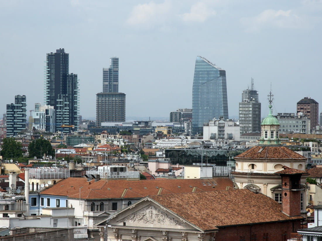 Milan skyline view featuring historic tile roofs in the foreground and modern glass skyscrapers of Porta Nuova in the distance