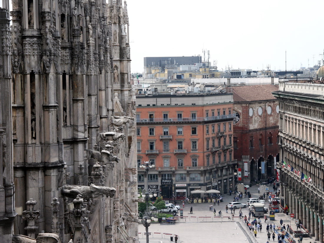 View from Milan Duomo rooftop terraces looking down at the city streets through Gothic gargoyles and spires