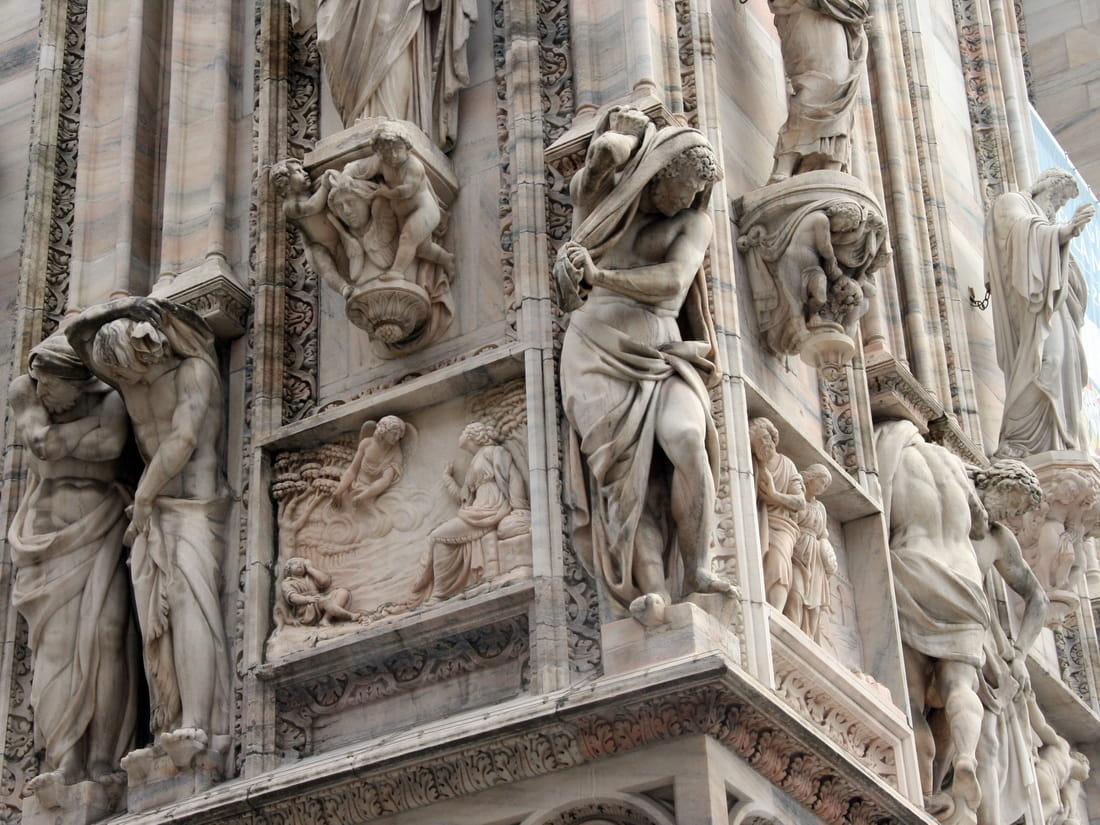 Close-up of intricate marble statues and reliefs on the facade of Milan Cathedral, showing biblical scenes and saints