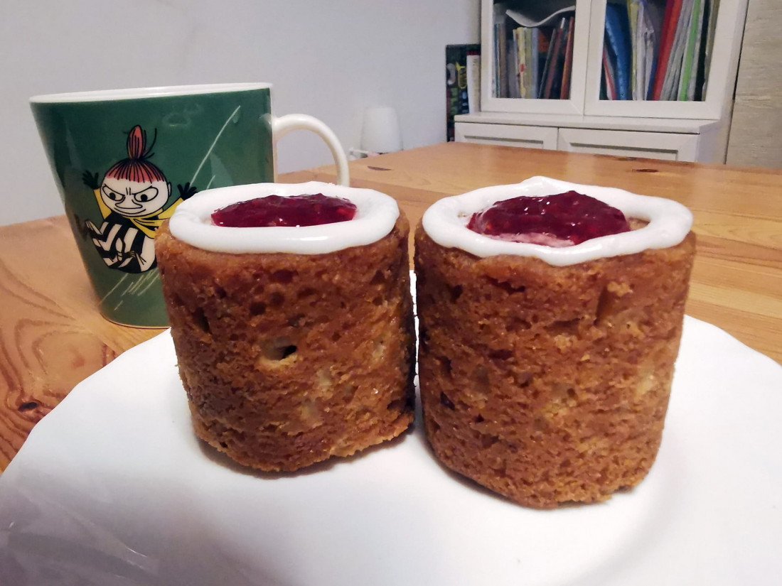 Two Runeberg tortes on a white plate next to a green Moomin mug, a cozy detail of Finland winter travel.