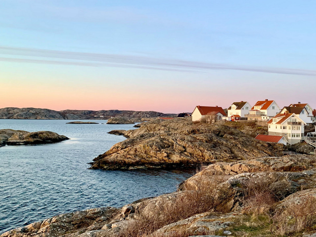 Scenic view of a coastal village on a Baltic Sea island with white and red houses perched on rocky terrain during a pink sunset.
