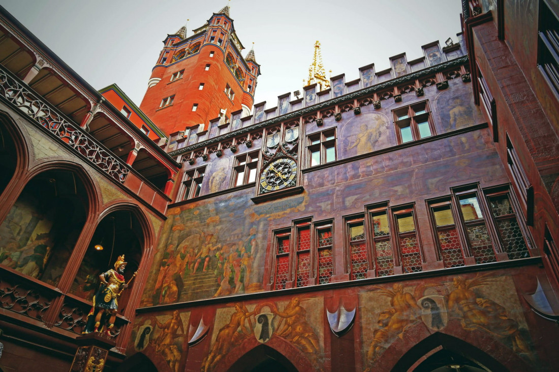 Inner courtyard of the Basel Town Hall (Rathaus) featuring ornate red facades, historical frescoes, and a golden statue