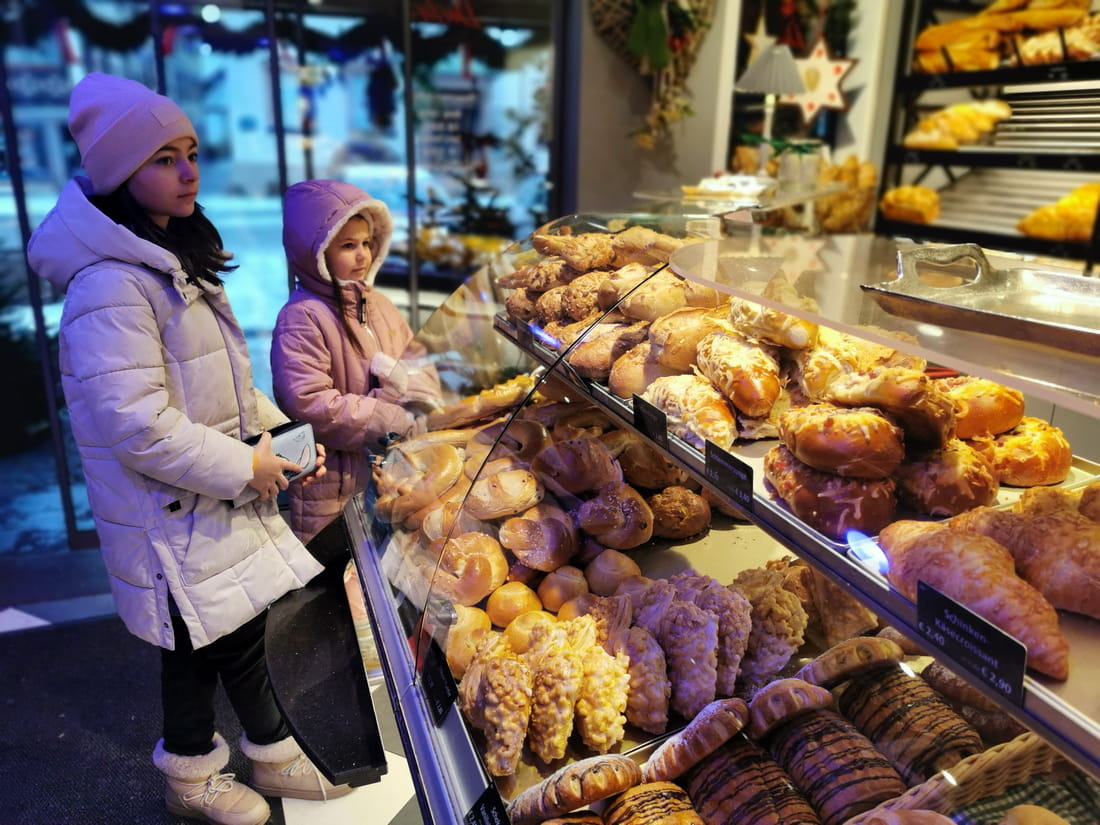 Children looking at fresh pastries and pretzels in a traditional German bakery window in Gengenbach during winter.