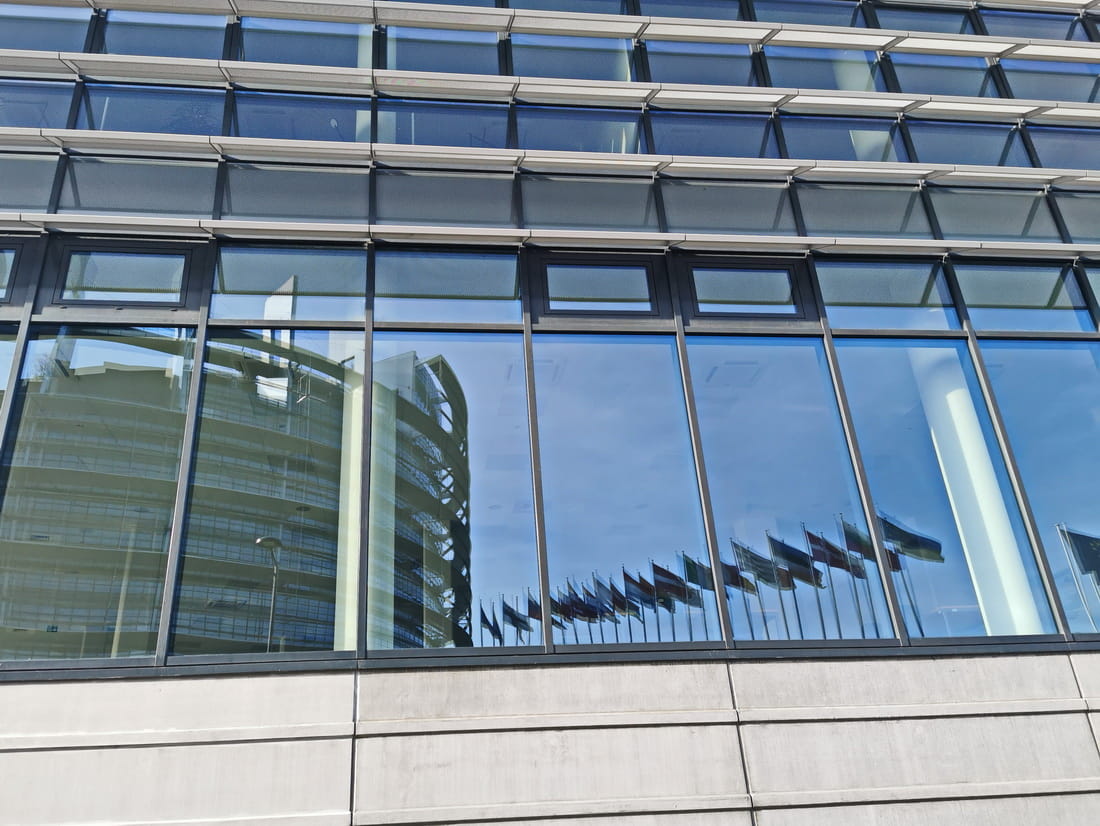 Reflection of the European Parliament tower in the modern glass windows of an office building.