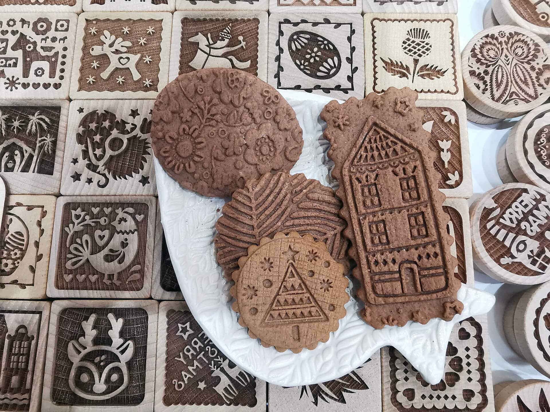 Freshly baked gingerbread cookies showing intricate house and geometric patterns, surrounded by square wooden baking stamps.