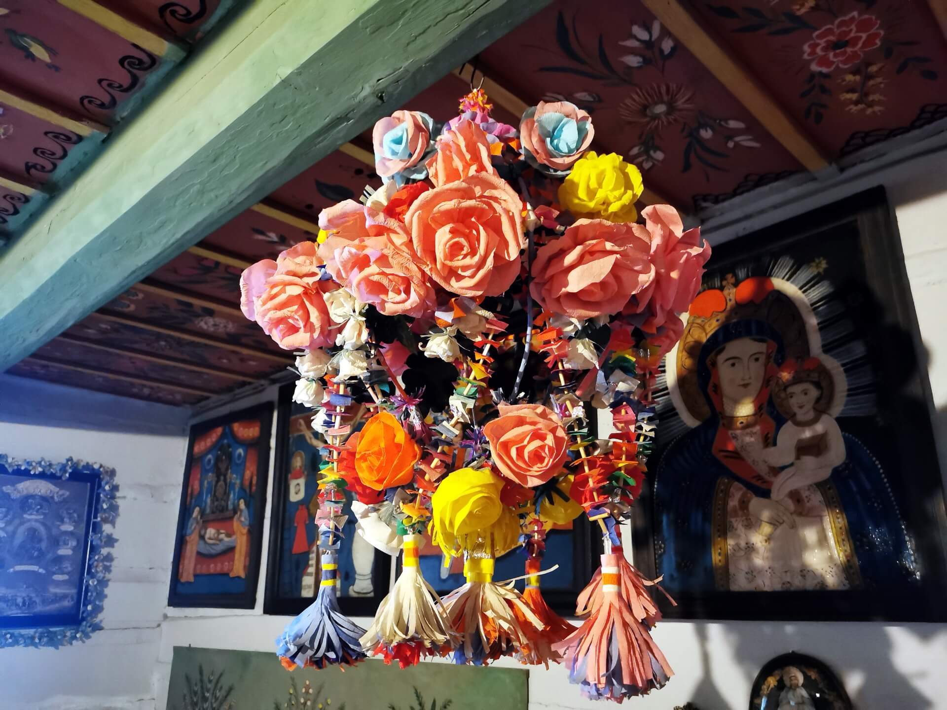 Traditional Polish paper flower chandelier hanging in front of a colorful folk painting of the Virgin Mary.