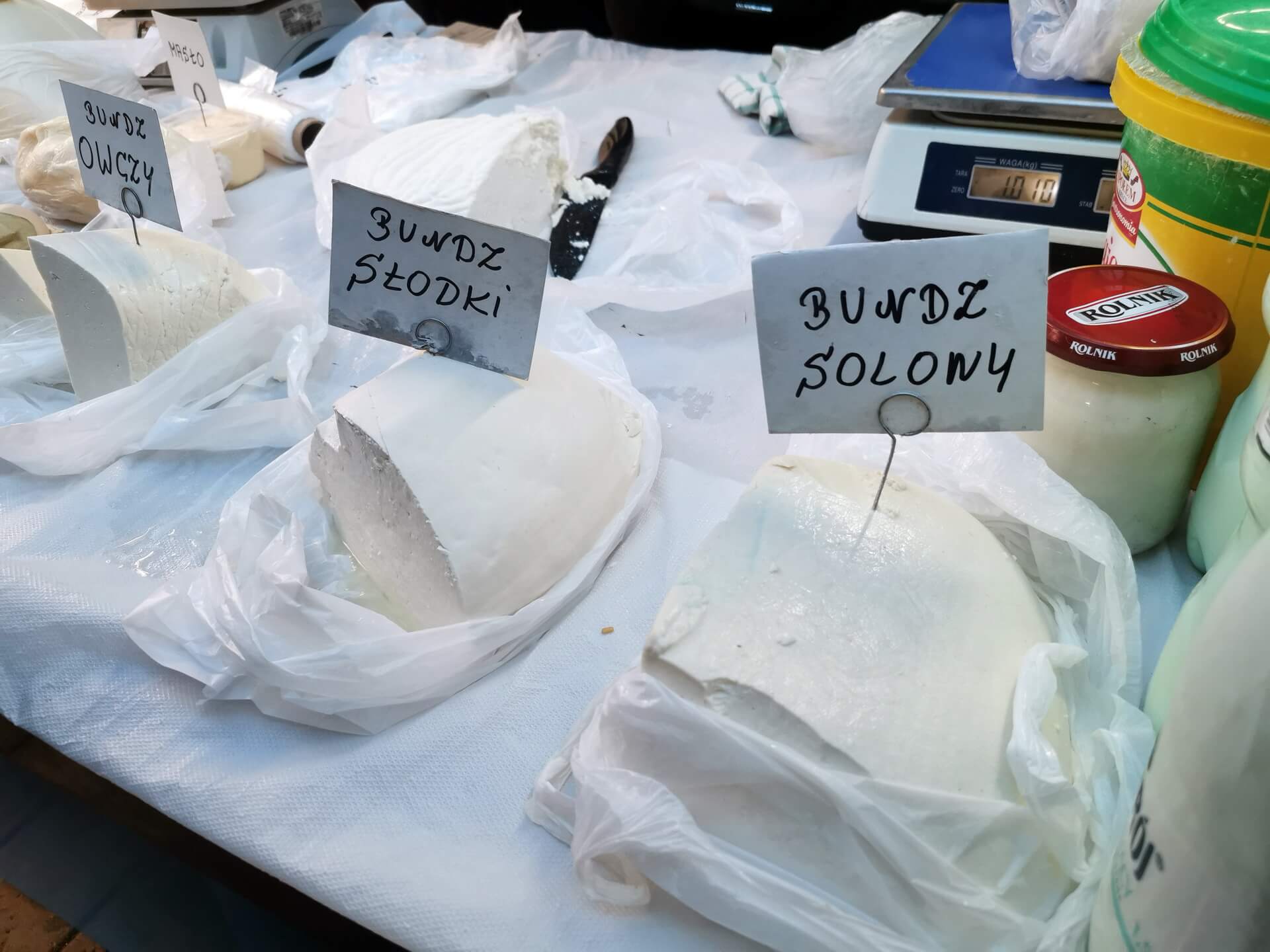Large blocks of fresh white bundz sheep cheese in plastic bags on a traditional Polish market stall.