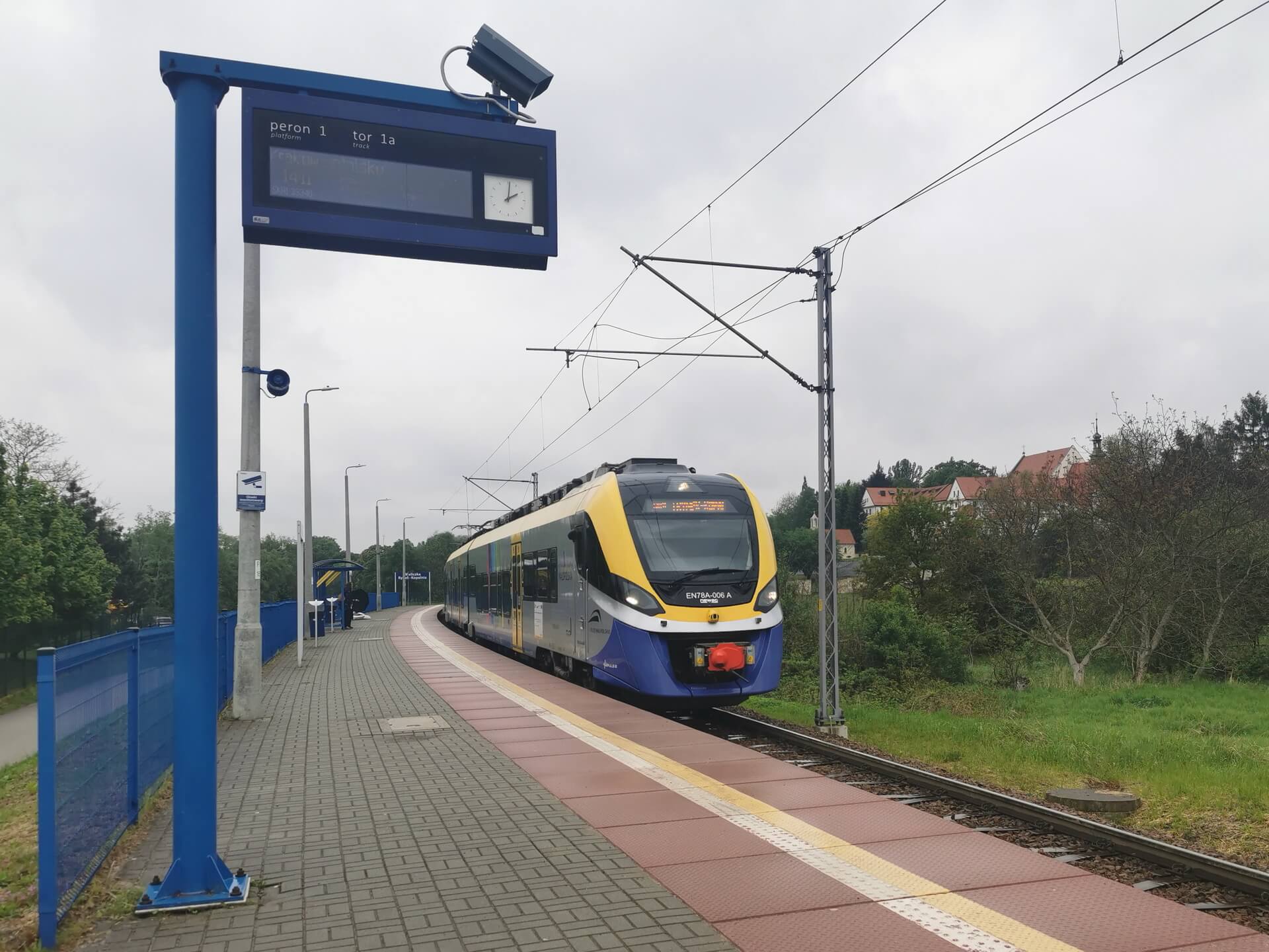 Modern regional train arriving at a rural station platform surrounded by greenery in Lesser Poland.