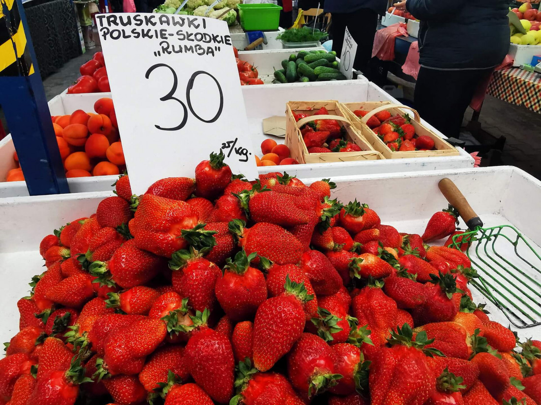 Mound of fresh seasonal strawberries with a handwritten price tag and a green scoop at Stary Kleparz market in Krakow.