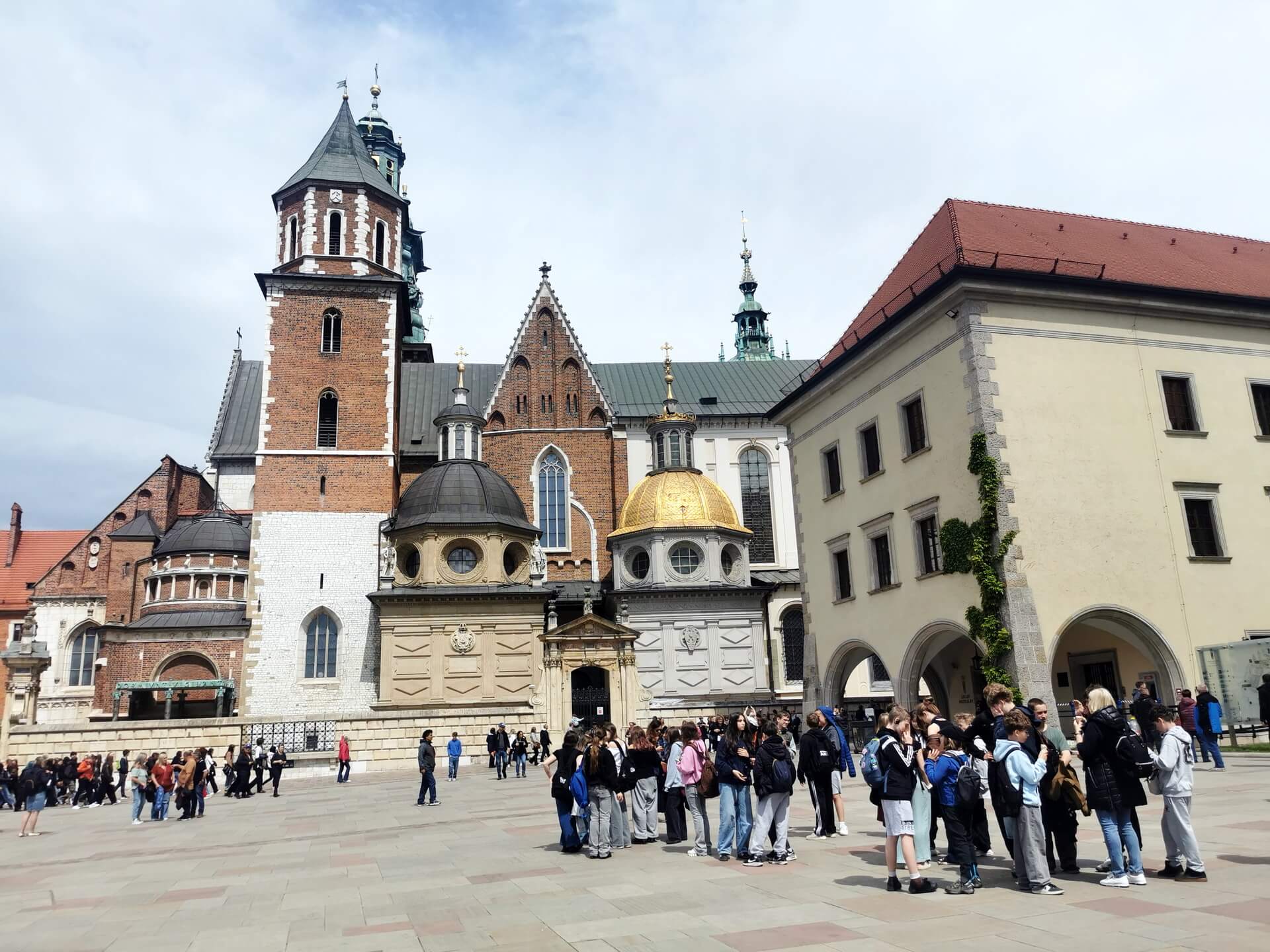 Large groups of tourists and school excursions gathered in front of the Wawel Cathedral in Krakow.