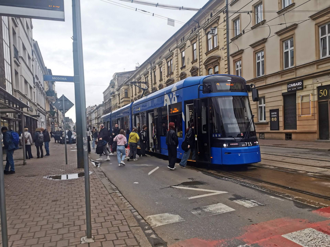 A blue public tram boarding passengers on wet Miodowa street in Kraków's Kazimierz district.