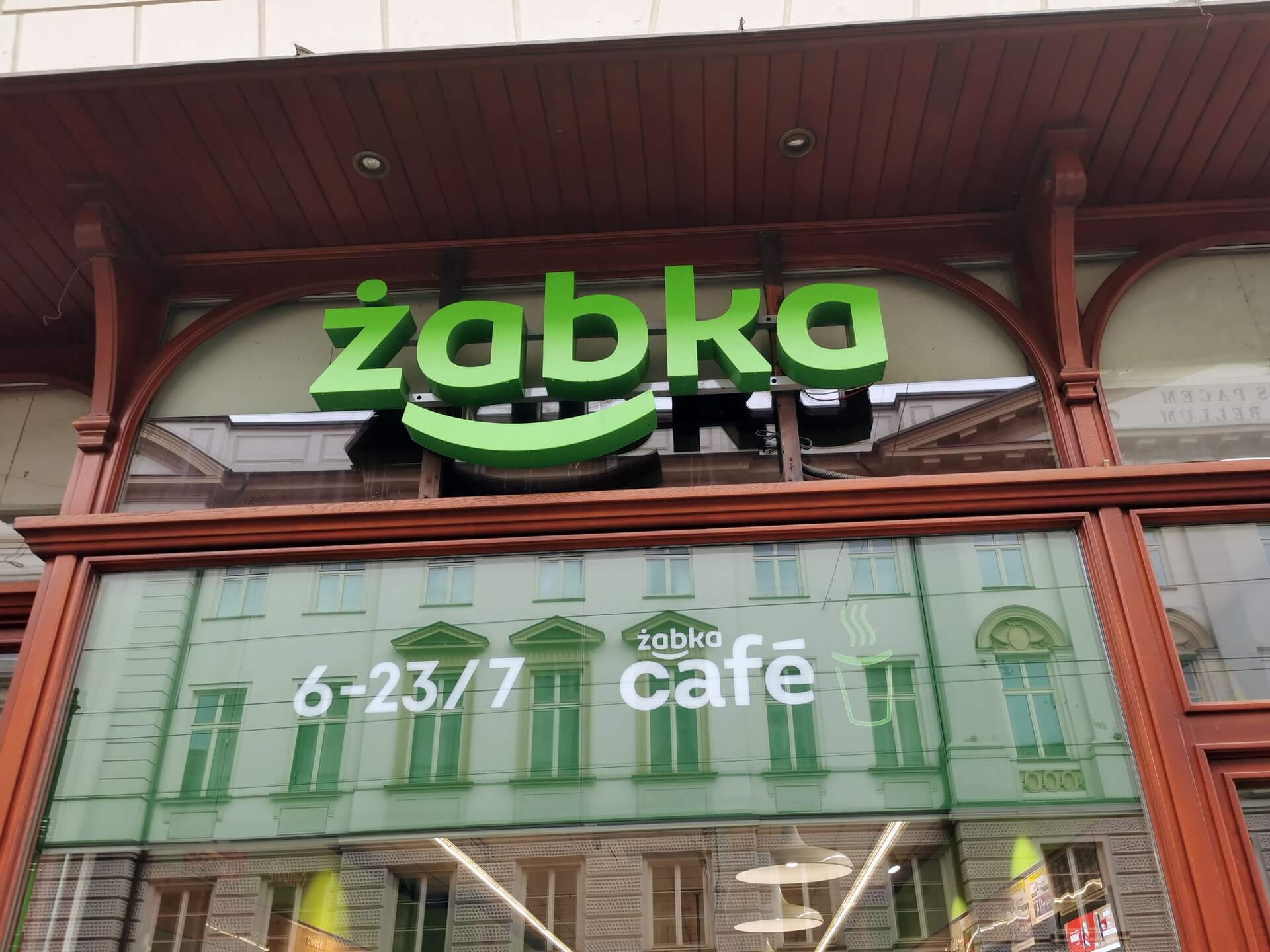 Green storefront of a Zabka convenience store in Poland showing opening hours from 6:00 to 11:00.