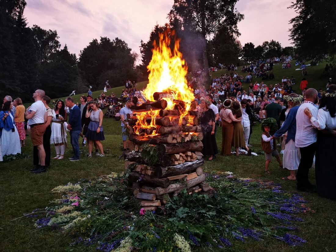 A massive Midsummer bonfire blazing at Turaida Castle in Latvia grounds with crowd in traditional crowns at twilight.